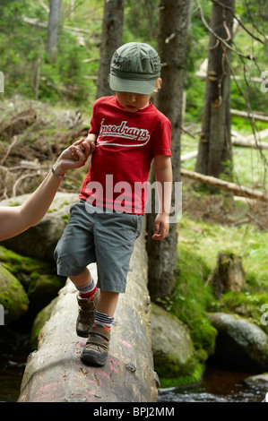 I bambini ad esplorare nella foresta - madre aiutare figlio oltre il torrente - parco nazionale Sumava Repubblica Ceca Foto Stock