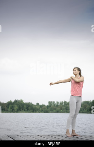 Giovane donna stretching su un molo al lago di Starnberg, Baviera, Germania Foto Stock