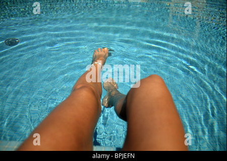 Donna dondolando le gambe in acqua, seduto sul bordo di una piscina Foto Stock