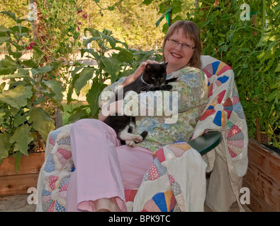 Questo Caucasian età matura donna nella sua 40's sorride tenendo premuto e petting il suo gatto nero pet. Essi sono qui seduti insieme Foto Stock