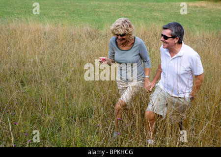 Un paio di pensionati fuori per una passeggiata attraverso un campo, tenendo le mani. Foto Stock