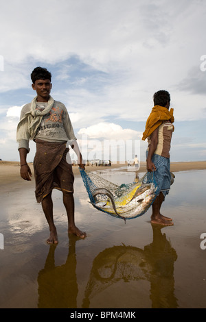 Due pescatori indiani portano qualche grosso pesce fresco catturato da net sulla spiaggia vicino al villaggio di pescatori. Foto Stock