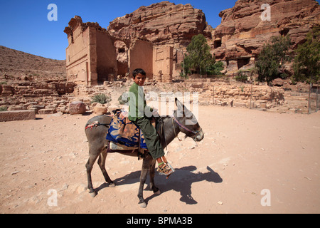 Bambino a cavallo di un asino di fronte al tempio di Dushares (Qasr al Bint), Petra, Giordania Foto Stock