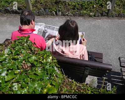 Coppia di mezza età lettura su una panchina nel parco REGNO UNITO Foto Stock