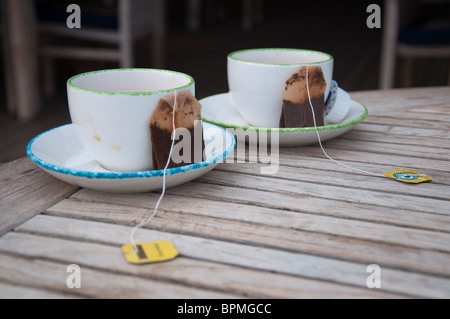 Due teacups vuoto con teabags utilizzati nei piattini su un tavolo di legno. Foto Stock