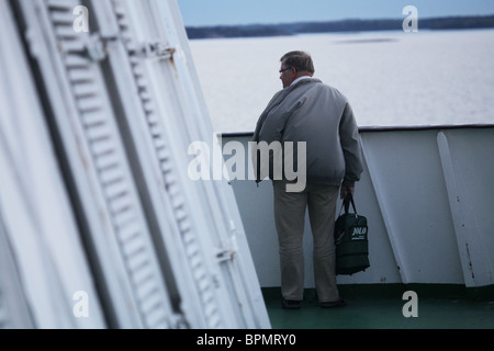 Un uomo in piedi sul ponte di un traghetto che naviga attraverso l'arcipelago finlandese sotto i cieli bui con una giacca da giorno ventosa che non soffia la faccia Foto Stock