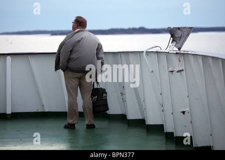 Un uomo in piedi sul ponte di un traghetto che naviga attraverso l'arcipelago finlandese sotto i cieli bui con una giacca da giorno ventosa che non soffia la faccia Foto Stock