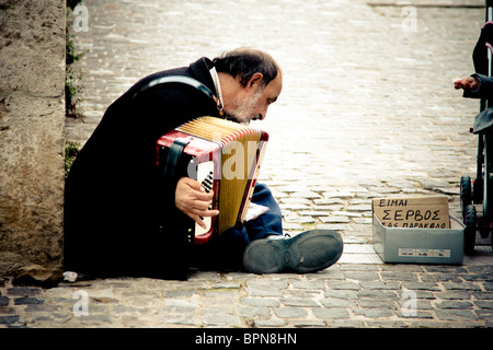 Vecchio immigrato serbo gioca per denaro per le strade di Atene in Grecia. Foto Stock