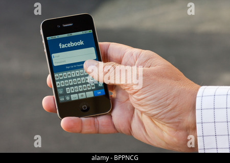 L'iPhone 4 nel palmo di una mano di un uomo, che mostra le app Facebook login. Foto Stock