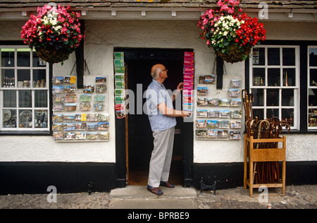 Un bottegaio rende le regolazioni finali alle sue scorte al di fuori del suo souvenir turistici business in Dunster High Street, Somerset. Foto Stock