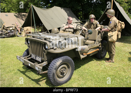 WW2 Membri Rievocazione della ventinovesima divisione di fanteria sedersi intorno a una Jeep Willys durante un weekend di ottenere insieme Foto Stock