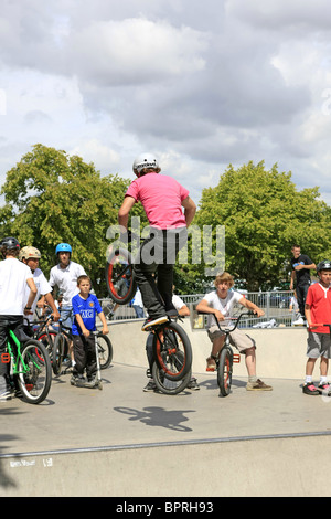 Un gruppo di ragazzi adolescenti guardare un amico maschio eseguire alcuni trucchi su una bmx bike a uno skateboard park Foto Stock