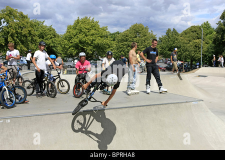 Un gruppo di ragazzi adolescenti guardare un amico maschio eseguire alcuni trucchi su una bmx bike a uno skateboard park Foto Stock