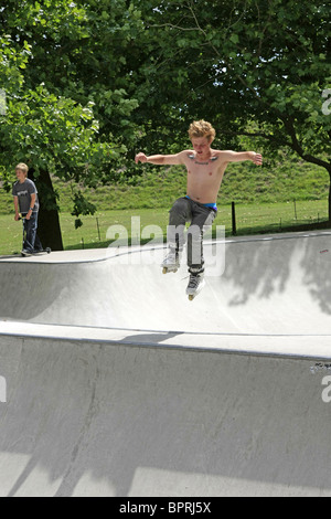 Ragazzo adolescente indossando roller-blade esegue il temerario acrobazie davanti ai suoi amici presso un parco di skateboard Foto Stock