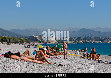 La folla sulla spiaggia ghiaiosa di Antibes e Villeneuve Loubet, guardando verso Nizza. Foto Stock