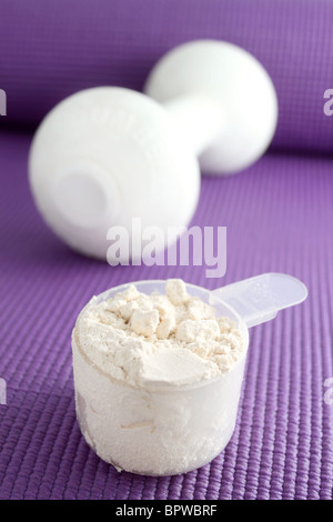 Un cucchiaio di polvere di vaniglia di proteina con dumbell in background su un esercizio di viola mat. Foto Stock