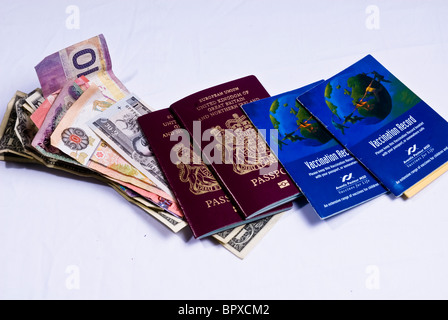 Regno Unito i passaporti e i libri di vaccinazione posa su varie banconote provenienti da tutto il mondo, compresi i dollari americani. Foto Stock