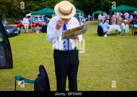 Un vecchio uomo in un diportista più paglia legge il Daily Telegraph newspaper attraverso un paio di occhiali. Foto Stock