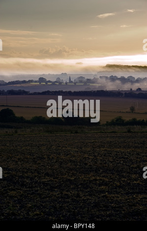 Nebbia di mattina passando sopra i campi con un villaggio di Dorset Foto Stock