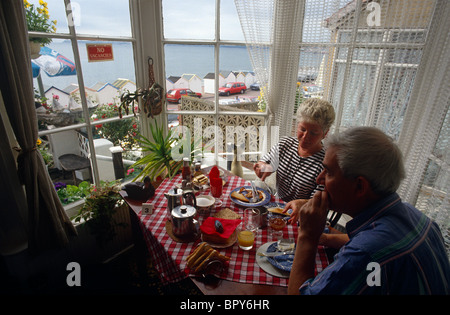 Coppia in vacanza godere di una completa colazione inglese colazione cotta nella finestra di baia di un Bed & Breakfast (B+B) nel Devon località balneare. Foto Stock
