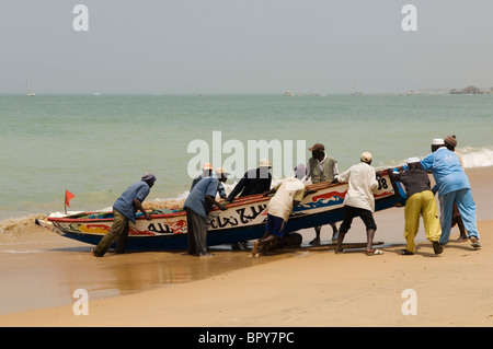 I pescatori la laminazione di una piroga fino alla spiaggia, Saly-Portugal, Petit Côte, Senegal Foto Stock