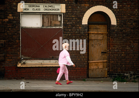 Una donna di mezza età cammina lungo un cupo street in Toxteth, Liverpool, in Inghilterra. Foto Stock