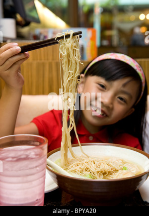 Giovane ragazza cinese di giocare con il cibo e mangiare wonton zuppa di noodle al ristorante Foto Stock