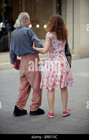 Uomo anziano instabile sui suoi piedi essendo aiutato a camminare lungo la strada Konigsalle, Dusseldorf, Germania. Foto Stock