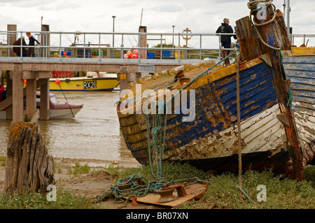 Abbandonata e abbandonato la pesca in barca sulle velme del porto di segale in East Sussex con nuova imbarcazione di salvataggio Jetty in background Foto Stock