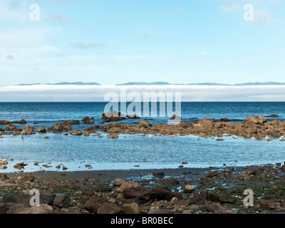 Spiaggia rocciosa & Tidal piscina sulla costa nord della Penisola Olimpica con vista dell'isola di Vancouver concealeled parzialmente dal basso nebbia banca Foto Stock