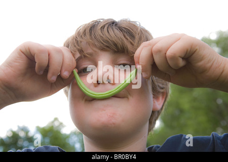 Ragazzo tenendo un fagiolo verde sul suo volto dichiara di avere un baffi closeup Foto Stock