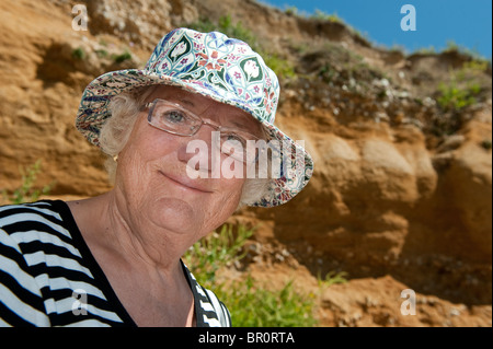 Signora anziana indossando un cappello seduti all'aperto su una giornata d'estate sorridente. Foto Stock