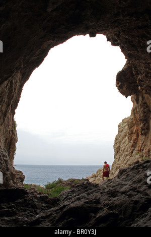 Un turista si erge di fronte all'apertura di una grande grotta accessibile da AlSamra spiaggia del nord western più punto di Siria Foto Stock