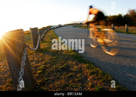 Una donna è il ciclismo su strada atsunset a Iona Beach, Richmond, British Columbia, Canada. Foto Stock