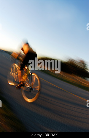 Una donna è il ciclismo su strada atsunset a Iona Beach, Richmond, British Columbia, Canada. (Sfumata movimento) Foto Stock