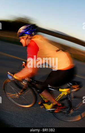 Una donna è il ciclismo su strada atsunset a Iona Beach, Richmond, British Columbia, Canada. (Sfumata movimento) Foto Stock