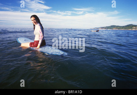 Una giovane donna seduta su una tavola da surf si è rivolta a guardare la fotocamera, Michoacan, Messico. Foto Stock