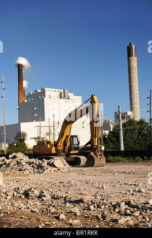 Sito industriale con un bulldozer in primo piano e fabbrica con fumaioli in background Foto Stock