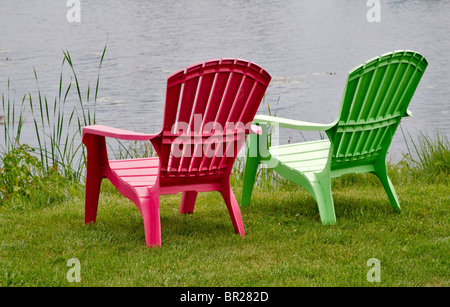 Due stile Adirondack sedie lounging in erba che guarda all'acqua. Esse sono realizzate delle colorate in plastica resistente Foto Stock