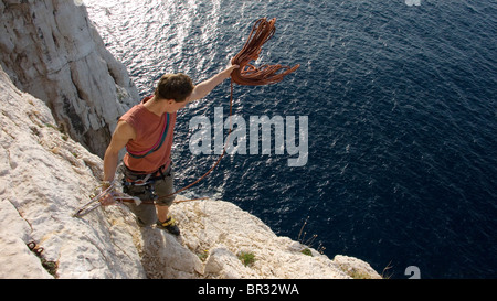 Rockclimber indossando un arancio tanktop getta una fune sulla rupe verso l'oceano. Foto Stock