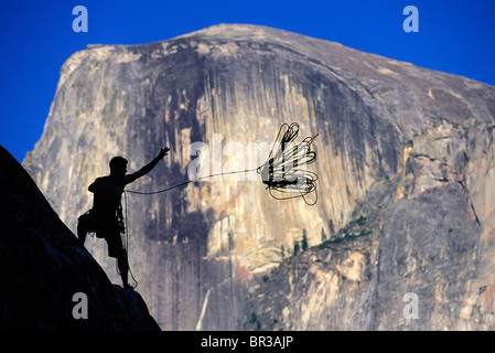 Silhouette contro una cupola di granito di uno scalatore di gettare una fune da un dirupo. Foto Stock