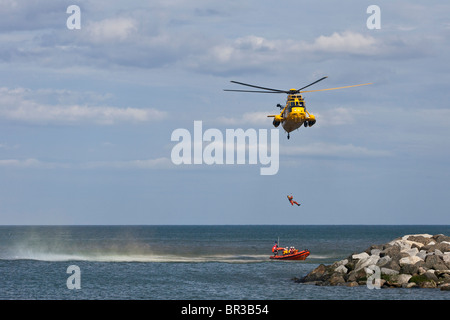 RAF Sea King Salvataggio in elicottero, abbassa una winchman in attesa di costiera RNLI scialuppa di salvataggio. Foto Stock
