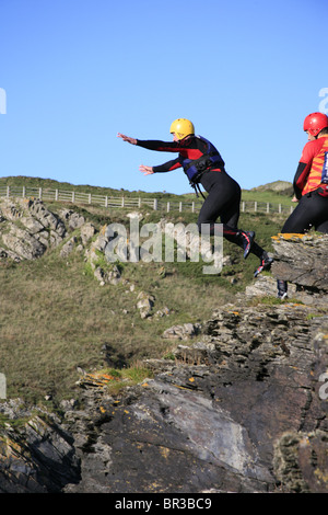 Coasteering Cornovaglia; Uomo salta fuori da una scogliera in mare Foto Stock