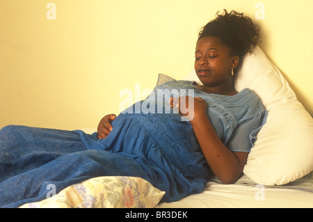 Incinta donna etnica giacente su un letto con le mani sulla sua pancia come se lei si sente il bambino muoversi Foto Stock