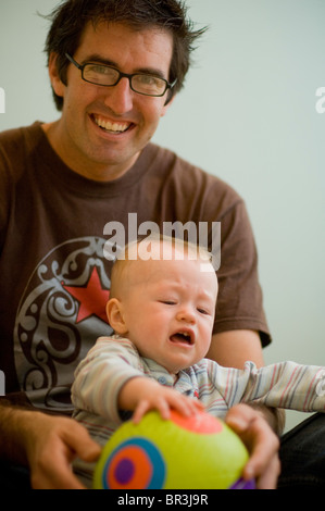 Sorridente uomo maturo detiene il bimbo che piange e sfera Foto Stock