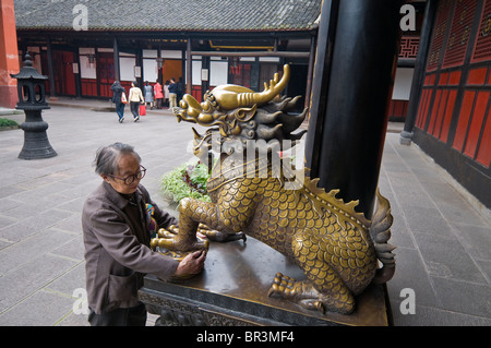 Anziani adoratore di carezze leone di ottone per migliorare la salute, Tempio Wenshu, Chengdu nella provincia di Sichuan, in Cina Foto Stock