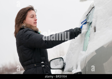 Giovane donna di pulizia vetri auto da neve nella stagione invernale Foto Stock