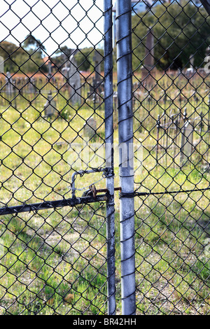 Bloccato cancello del cimitero con le lapidi in distanza Foto Stock