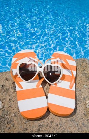 Striped flip flop e a forma di cuore ad occhiali da sole in piscina Foto Stock