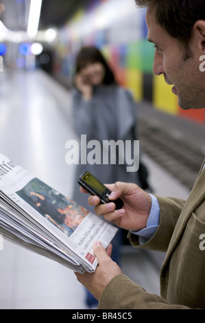 L'uomo presso la stazione della metropolitana con giornali e telefono cellulare Foto Stock